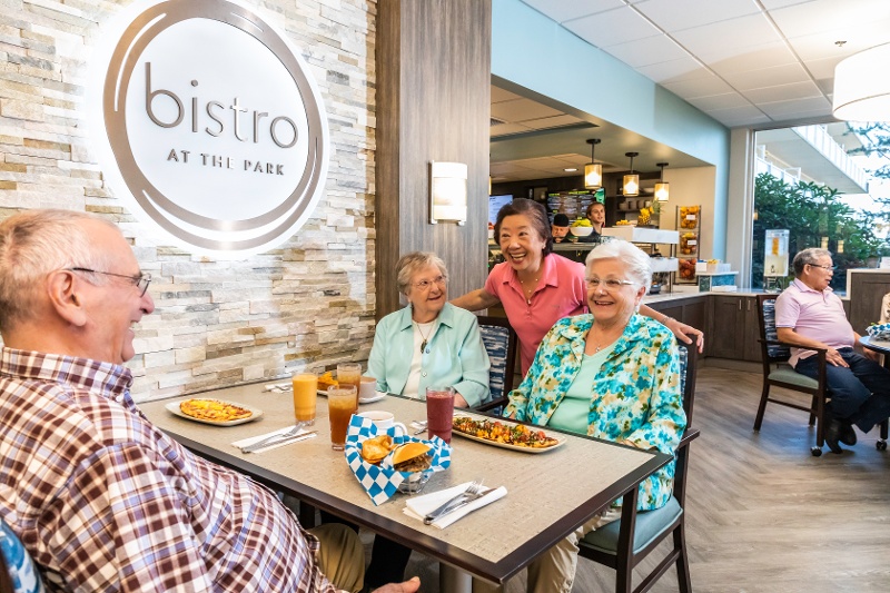 A table of people laughing as they eat hamburgers, flatbread pizza, and smoothies.